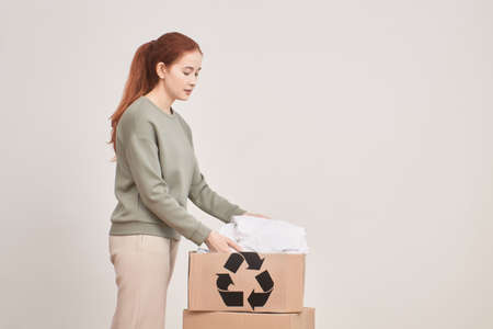 girl puts things in a box for recycling, second hand, eco concept, girl against a white wall
