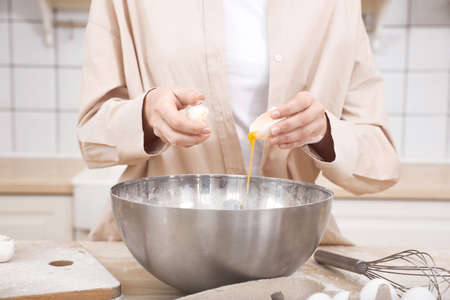 Female hands break an egg in the kitchen into a bowl for cooking.の写真素材