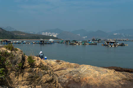 Fisherman fishing with rod, in front of sok kwu wan on Lamma Island Hong Kongの写真素材