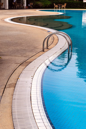 Curved poolside of a fresh blue swimming pool with stairs. The pool steps are in line with the curve of the pool.のeditorial素材