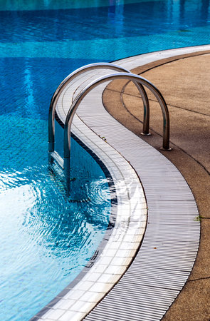 Curved poolside of a fresh blue swimming pool with stairs. The pool steps are in line with the curve of the pool.のeditorial素材