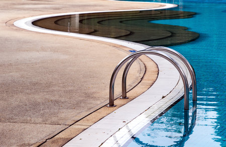 Curved poolside of a fresh blue swimming pool with stairs. The pool steps are in line with the curve of the pool.のeditorial素材