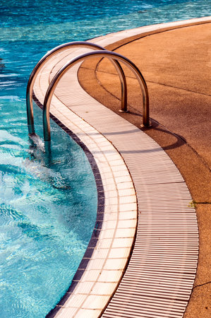 Curved poolside of a fresh blue swimming pool with stairs. The pool steps are in line with the curve of the pool.のeditorial素材