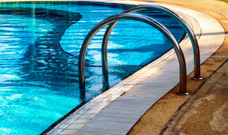 Curved poolside of a fresh blue swimming pool with stairs. The pool steps are in line with the curve of the pool.のeditorial素材