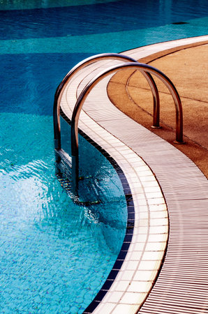 Curved poolside of a fresh blue swimming pool with stairs. The pool steps are in line with the curve of the pool.のeditorial素材