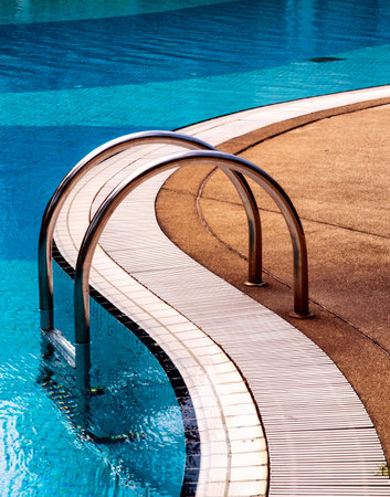 Curved poolside of a fresh blue swimming pool with stairs. The pool steps are in line with the curve of the pool.のeditorial素材