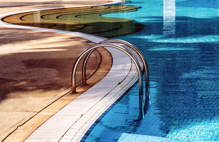Curved poolside of a fresh blue swimming pool with stairs. The pool steps are in line with the curve of the pool.のeditorial素材