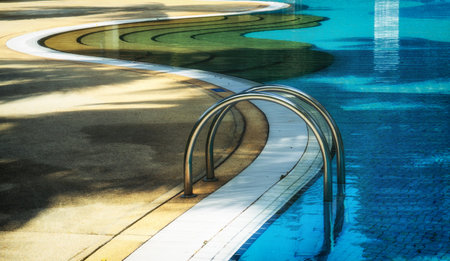 Curved poolside of a fresh blue swimming pool with stairs. The pool steps are in line with the curve of the pool.のeditorial素材
