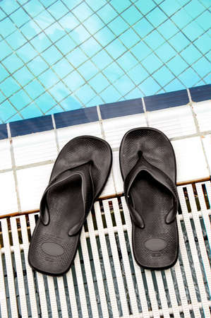 Pair of black sandals on the poolside.  The pool has fresh blue water.の写真素材