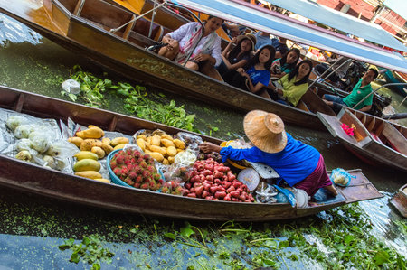 A lady selling fruit from her boat at a floating market in Thailand. Image taken at Damnoen Saduak floating market near Bangkok.のeditorial素材