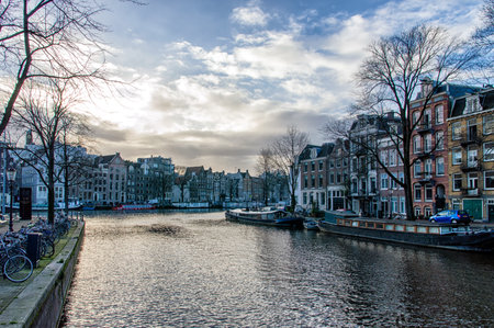 This is a landscape image of a canal in Amsterdam, Netherlands. Several boats along the water are visible within the shot.のeditorial素材