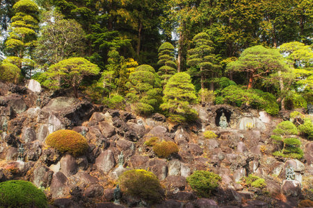 Narita, Japan 17 March, 2018: bonsai trees growing outdoor in a garden on a slope with a statue sitting in a small cave, Naritasan Temple, Narita, Japanのeditorial素材