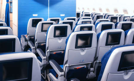 Modern aircraft interior with seats and blank touch entertainment screens displays. Concept of fast...