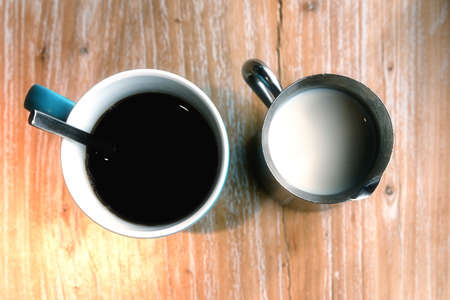 Ceramic coffee mug with steel creamer decanter  set on wooden tableの写真素材