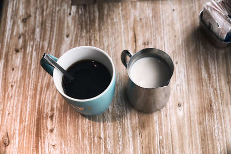 Ceramic coffee mug with steel creamer decanter  set on wooden tableの写真素材