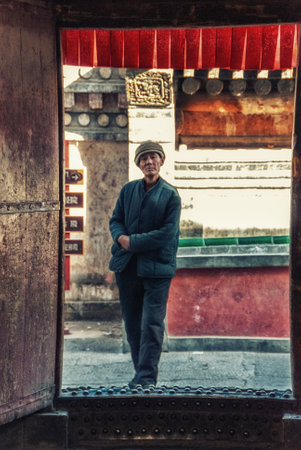 Xining, China - 25 December 2009: Old male lama walk in front of traditional brick wall in the...
