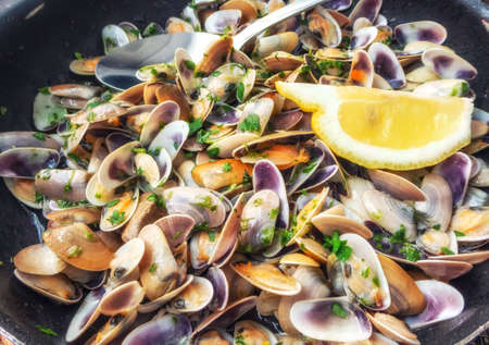 Close-up view of clams in green sauce, with half of a lemon on top. The clams in green sauce are prepared with white wine, olive oil, garlic and parsley.の写真素材