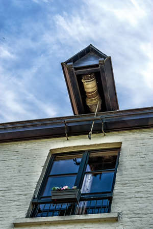 Closeup of slanted pulley hook and beam at gable on top of white brick house under blue sky.の写真素材