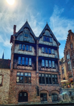 Dark brown wooden facade among other brown brick stone facades along black water canal, Brugge, Belgiumのeditorial素材