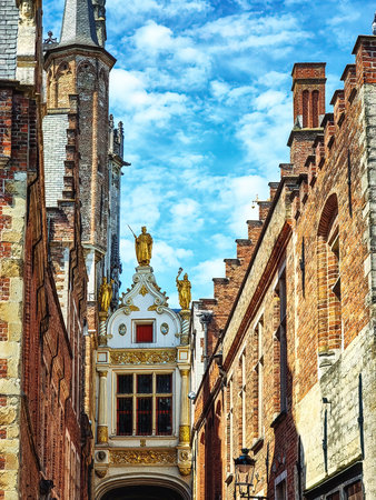 A white bridge connecting two typical Flemish buildings with golden statues and details in Brugge, Belgiumのeditorial素材