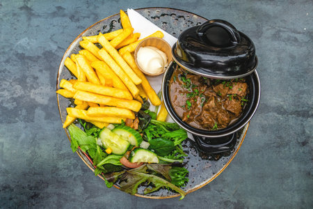 Top view of sour meat (Dutch: Zuurvlees) served with french fries (friet or patat ) and mixed salad, Is a regional meat dish from Limburg, Province that exists in both the Netherlands and Belgium.の写真素材
