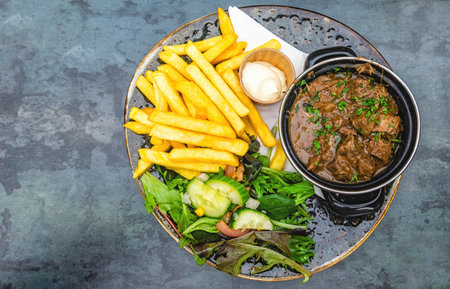 Top view of sour meat (Dutch: Zuurvlees) served with french fries (friet or patat ) and mixed salad, Is a regional meat dish from Limburg, Province that exists in both the Netherlands and Belgium.の写真素材