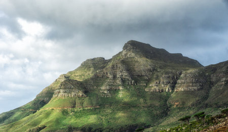 scenic landscape of cloudy sky covering the peak of Table Mountain in Cape Town on a sunny morning from below. Beautiful views of plants and trees around an iconic natural landmarkの写真素材
