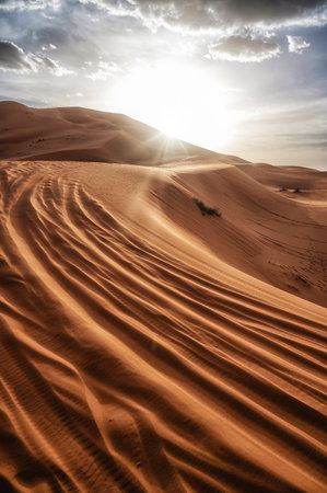 Desert dunes landscape with sun flare on cloudy sky background, Sahara, Moroccoの写真素材
