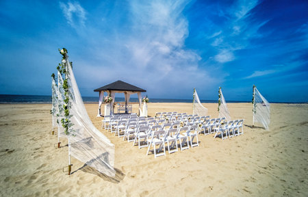 Wedding altar and row of white chairs prepared on the beach against a background of beautiful sea and blue sky. Destination wedding and celebration in a tropical country concept.の写真素材