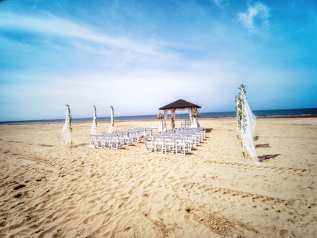 Wedding altar and row of white chairs prepared on the beach against a background of beautiful sea and blue sky. Destination wedding and celebration in a tropical country concept.の写真素材