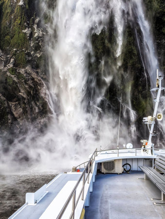 Tourist boat approaching mighty Lady Bowen Falls a 164 meter waterfall in Milford Sound Fjordland South Island New Zealandの写真素材