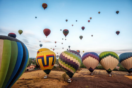 Colorful hot air balloons about to take off at dawn in rural field with blue sky near the town of Teotihuacan, Mexico.の写真素材