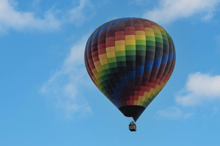 A vibrant, multicolored hot air balloon soars in a clear blue sky during a sunny dayの写真素材
