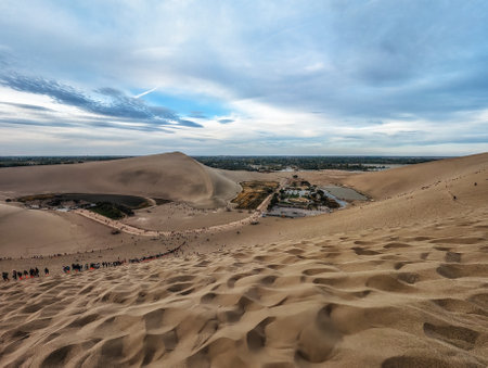 Tourists climbing Mingsha Mountain (Echo Sand Mountain) a sand mountain range about 40km in length, 20km in width. The highest altitude is 1650m. It's one of the top attractions in Dunhuang, Gansu province, Chinaの写真素材