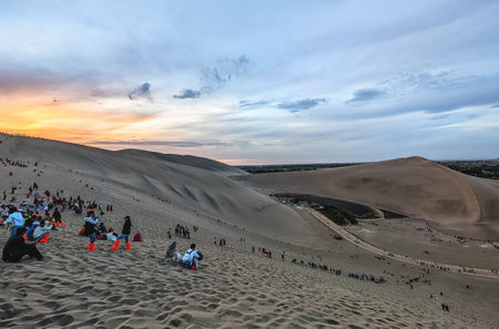 Tourists climbing Mingsha Mountain (Echo Sand Mountain) a sand mountain range about 40km in length, 20km in width. The highest altitude is 1650m. It's one of the top attractions in Dunhuang, Gansu province, Chinaの写真素材