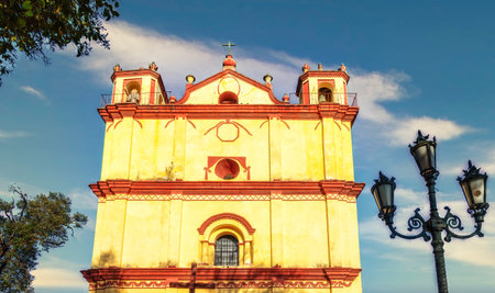 The vibrant yellow and terracotta facade of the historic Iglesia de San Francisco, Church of St. Francis, stands against a partly cloudy sky in San Cristobal de las Casas, a colonial city in Chiapas, Mexico.の写真素材