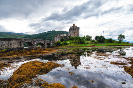 Eilean Donan Castle stands majestically amid autumn hues, its reflection shimmering in calm waters....