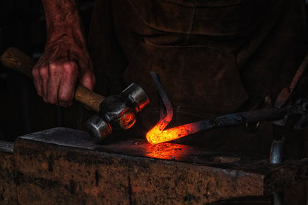The blacksmith manually forging the molten metal on the anvil in smithy with sparks