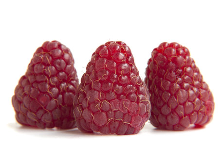 three red raspberries on a white background