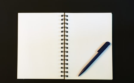 white pages of an open notebook and a pen on a black background