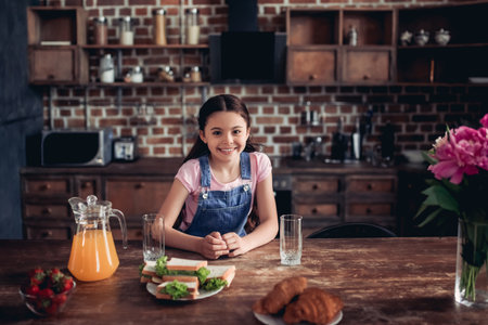 portrait of smiling girl looking at the camera while sitting at the kitchen table with breakfast on the kitchenの写真素材