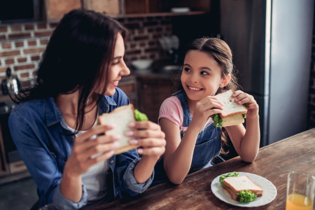 portrait of smiling mother and daughter holding sandwiches and looking at each other in the kitchenの写真素材
