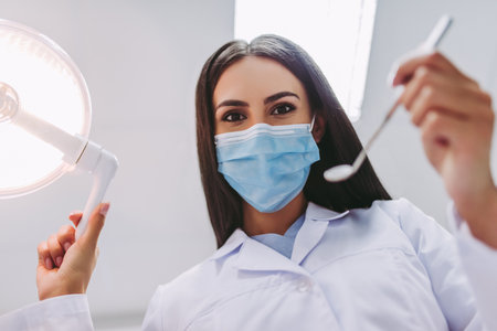 low angle view of dentist in medical mask holding dental tools in modern dental clinicの写真素材