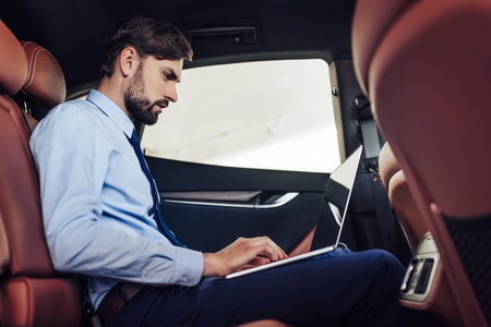 side view of caucasian businessman using laptop computer in the car