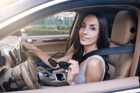 portrait of brunette woman holding sunglasses and looking at the camera while sitting in the car