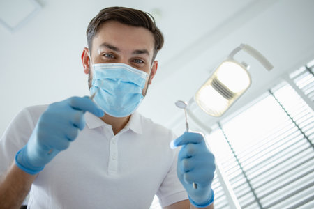 low angle view of male dentist checking patient teeth with mirror in modern clinicの写真素材