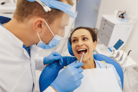 Overhead shot of male dentist in protective mask examining client teeth with dental tools in clinicの写真素材