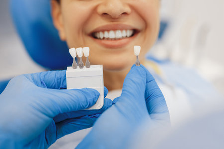 Cropped shot of dentist hands in rubber gloves holding teeth color palette with smiling client on background. medical conceptの写真素材