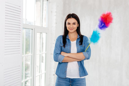 Admirable woman in denim standing with crossed arms and holding dust removing stickの写真素材