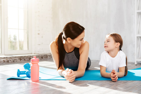 Delighted woman looking at her child with love while resting on fitness matの写真素材